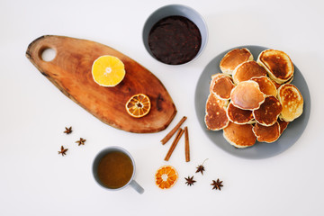Lush pancakes and teapot with spices, cup of tea with orange, cinnamon, anise. Tasty breakfast on white background. Good morning