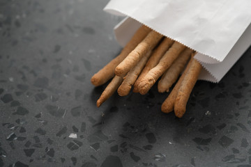 Traditional italian snack - grissini in white paper bag on concrete surface