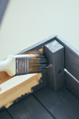 Wooden brush and a can of gray paint next to a wooden box on craft paper. Close-up, selective focus.