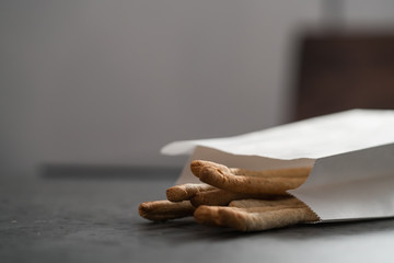 Traditional italian snack - grissini in white paper bag on concrete surface