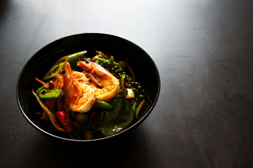 Stir fried seafood in black bowl on dark gray background