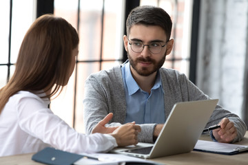 Close up focused businessman listening businesswoman talking in boardroom at meeting. Leader presenting new business concept for male colleague discuss. Team together using laptop for teamwork.