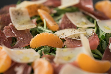 Salad with prosciutto, tangerines and vintage cheese closeup