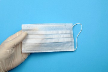 Hand in a medical glove holds a disposable mask on a blue background.