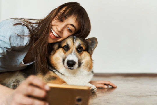 Portrait laughting young woman hugging cute Welsh Corgi dog dog and taking selfie with pet on smartphone camera. Concept stay at home, friendship with dog, taking picture.