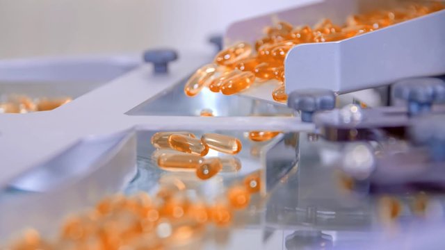Extreme closeup of orange gel pills falling into a machine during its production