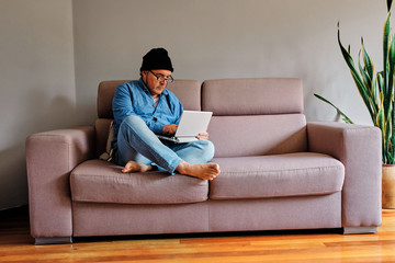 Casual dressed man working at home sitting on sofa with laptop