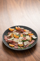 Salad with prosciutto, tangerines and vintage cheese on walnut table with copy space