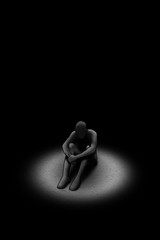 Person sitting alone in isolation feeling despressed in the dark with a spotlight shining on them
