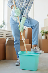 Vertical low section portrait of cheerful young woman cleaning new house or apartment while moving...