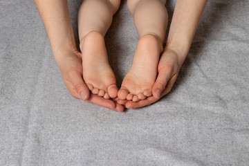 Small children's legs, heels in gentle affectionate mother's parental hands.
