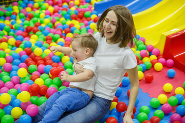 Fototapeta na wymiar child and mother on trampoline. smiling baby boy comes from a slide with mothers. funny family weekend in plaing centre. active family vacation indoor. mom and son have fun together on playground.