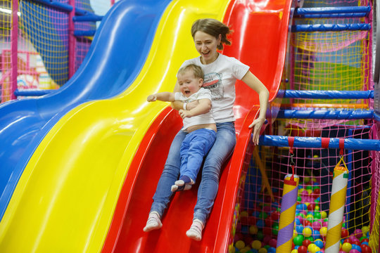 child and mother on trampoline.
smiling baby boy comes from a slide with mothers.
funny family weekend in plaing centre.
active family vacation indoor. mom and son have fun together on playground.