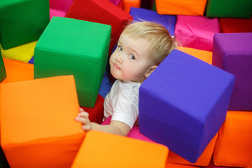 smiling child in playroom. funny baby boy in a pool with colorful soft toy cubes. family rest in the children's center. portrait a little boy have fun in playing room close up. happy childhood concept
