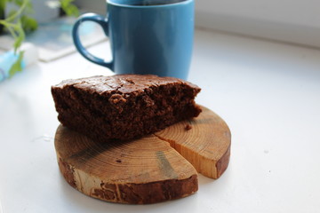 a piece of homemade chocolate cake lies on a wooden stand next to a mug a Cup of tea or coffee on a white background with a place to insert text