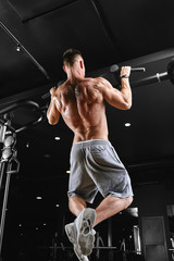 Strong man doing pull-ups on a bar in a gym.