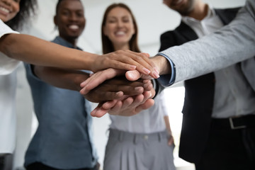 Close up happy diverse business people putting hands together, showing support and unity. Multiracial colleagues involved in team building activity. Staff training concept, start working together.