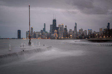 Obraz premium Fantastic cityscape panoramic skyline view of Chicago from Fullerton Avenue during a windy day with water cascading over a concrete pier at night just after sunset as lights begin to turn on in city.