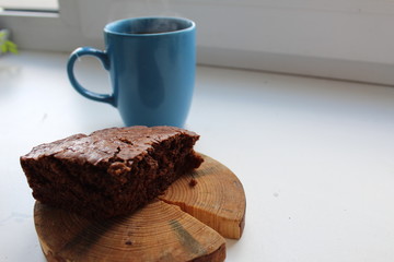 a piece of chocolate cake is placed on a wooden stand and there is a blue blue mug with a Cup of tea or coffee on a white background with a place for inserting text