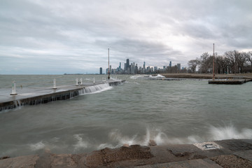 Fantastic cityscape panoramic skyline view of Chicago from Fullerton Avenue during a windy day with water cascading over a concrete pier at night just after sunset as lights begin to turn on in city.