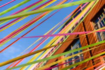 Multicoloured ribbons stream between buildings against a blue sky.