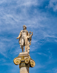 Apollo white marble statue on Ionian style column under blue sky with some clouds, Athens Greece