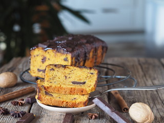 Pumpkin chocolate festive soft cupcake poured with chocolate icing with cut pieces and ingredients on a metal wire rack on a wooden ancient background.