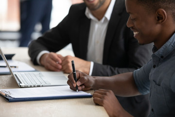 Close up happy african american businessman signing partnership agreement. Focused male on putting...