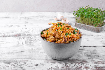 Pilaf with meat in a ceramic bowl on the white wooden table. Traditional oriental cuisine meal