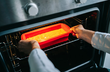 A woman puts a sponge cake in the oven to bake it