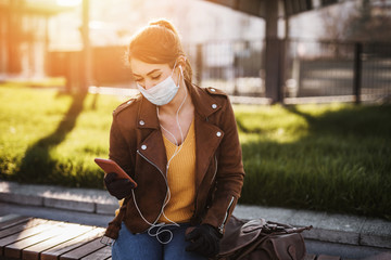 Young and elegant business woman walking on empty city street. She using phone while wearing protective mask to protect herself from dangerous virus. Corona virus or Covid-19 concept.