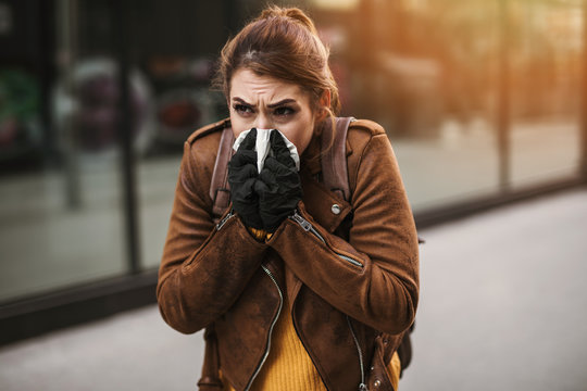 Elegant business woman infected and sick by virus standing on city street with protective mask, coughing and sneezing. Corona virus or Covid-19 lifestyle concept.