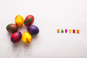 Multi-colored wooden letters making up the words happy easter and decorative colourful eggs on a white background.