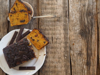 Festive pumpkin chocolate soft muffin, poured with chocolate icing with cut pieces on a white plate...
