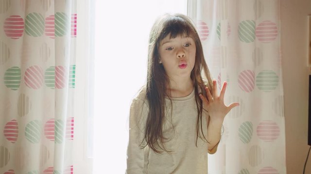 Funny expressive cute artsy little girl with long hair poses, dance near window