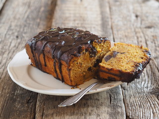 Festive pumpkin chocolate soft muffin, poured with chocolate icing with cut pieces on a white plate on a wooden background.