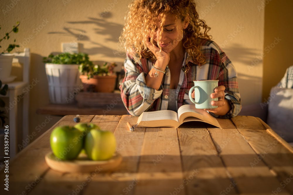 Wall mural beautiful curly adult woman read a book outdoor at home int errace or trendy room with wood table an