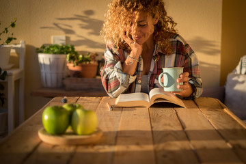 Beautiful curly adult woman read a book outdoor at home int errace or trendy room with wood table...