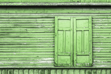 Rustic window in wooden village cottage house. Closed shutter grunge green wood wall. Countryside architecture background. Empty copy space peeling paint texture.