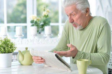 Portrait of emotional senior man reading newspaper