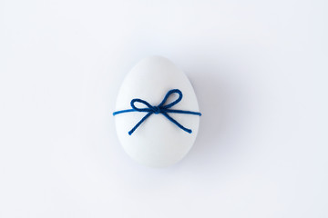 White egg with blue wool thread ribbon on white background
