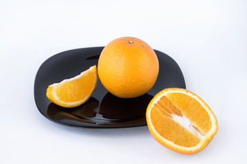 Juicy tasty orange, cutted orange on black plate on white background isolated