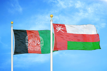 Afghanistan and Oman  two flags on flagpoles and blue cloudy sky