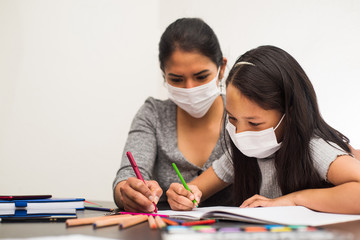 Latin mother helps her daughter with the homework on a black table at home, wears prevention mask. Teleworking and studying at home during coronavirus infection.