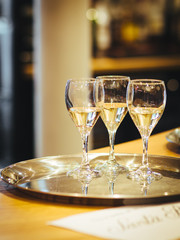 Interior shot of three glasses of white wine on a silver metallic tray placed on the table with blurred background in artificial lightning.