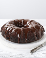 Homemade Chocolate bundt cake with melted chocolate on white background with copy space. Close up view, vertical composition, selective focus.