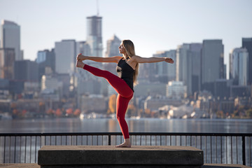 Fototapeta na wymiar Beautiful Woman Standing Yoga Pose Revolving Extended Hand to Foot in Front of City Skyline