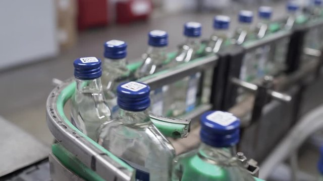 Row of bottles with vodka in conveyor belt in factory production line. Factory for bottling alcoholic beverages. Glass bottles in conveyor belt in distillery production line.