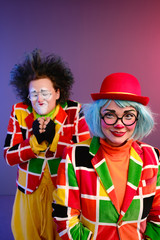 Two clowns a man and a woman with makeup in bright colored costumes are fooling around and showing a presentation