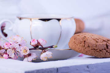 White porcelain cup of tea, milk jug, and fresh-baked oat cookies. English breakfast still-life with drink and treats and tablecloth.